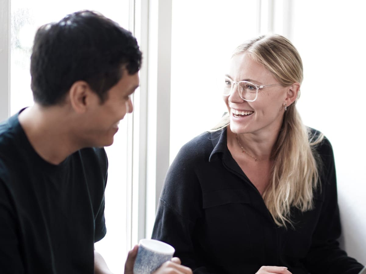 Two figures sitting and discussing work. Smiling and talking.