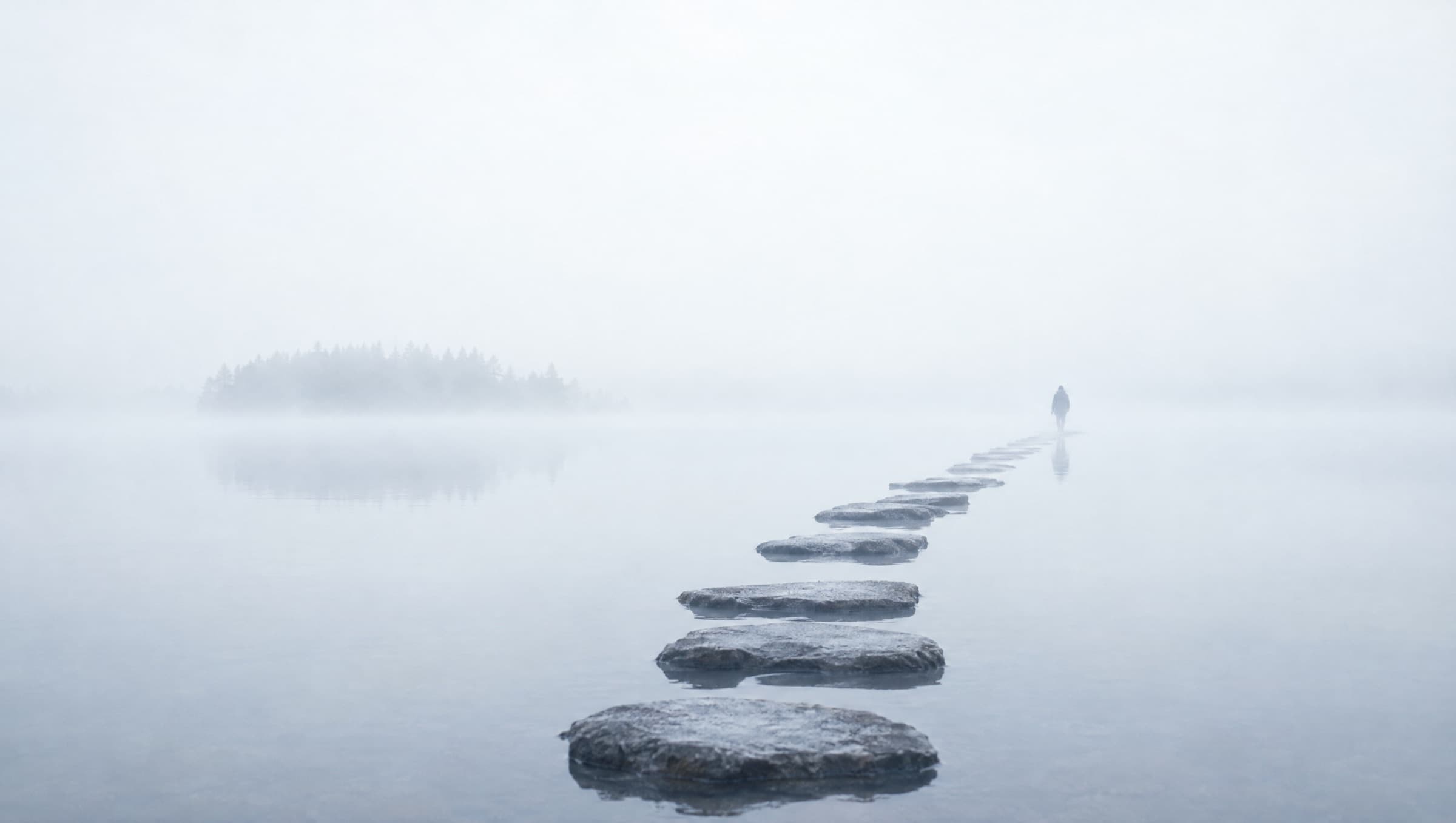 Stepping stones leading across a still lake into fog