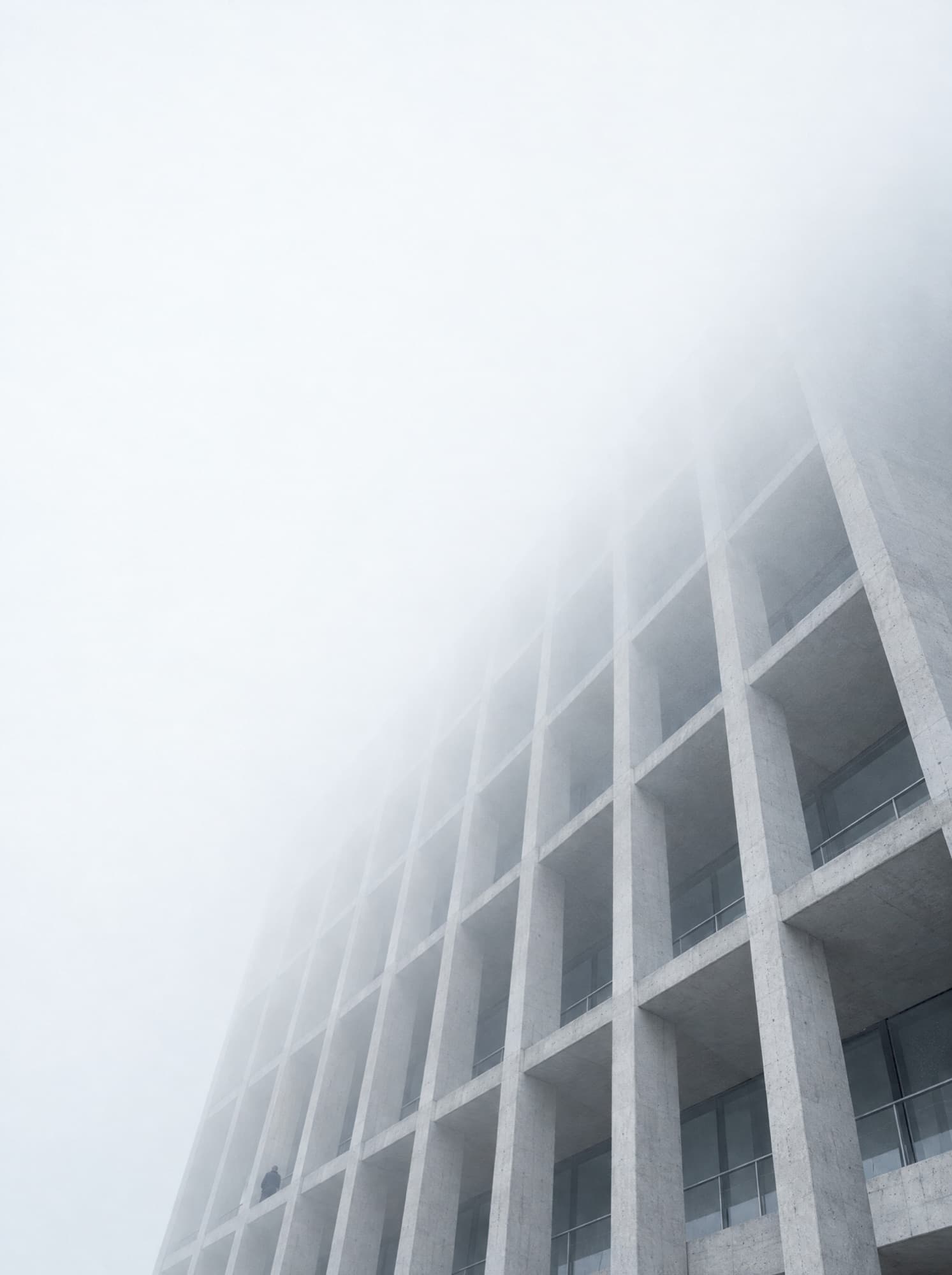 A modernist concrete facade disappearing into low cloud