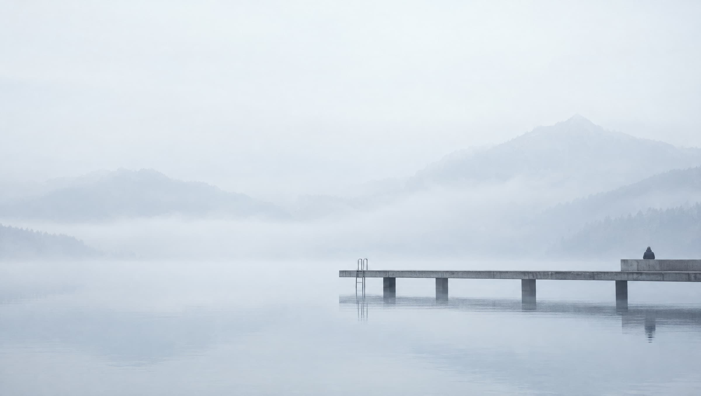 A concrete pier reaching into a still mountain lake in morning fog