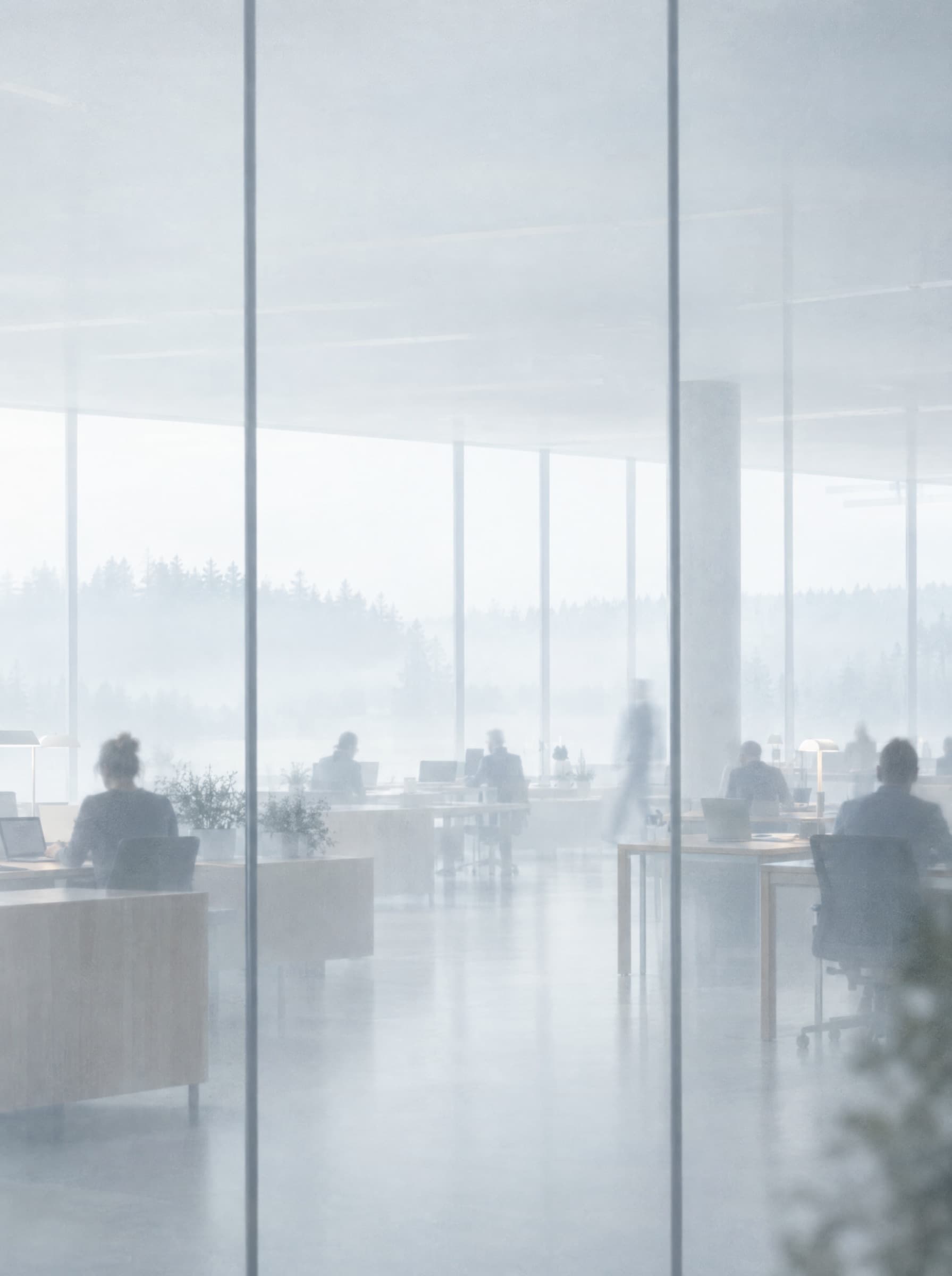 A bright open-plan office seen through tall frosted glass, people at work