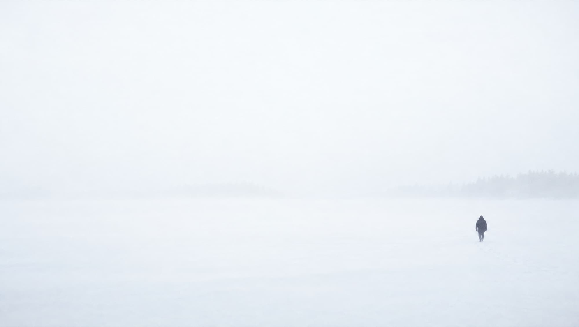 A lone figure walking across a snowfield in whiteout