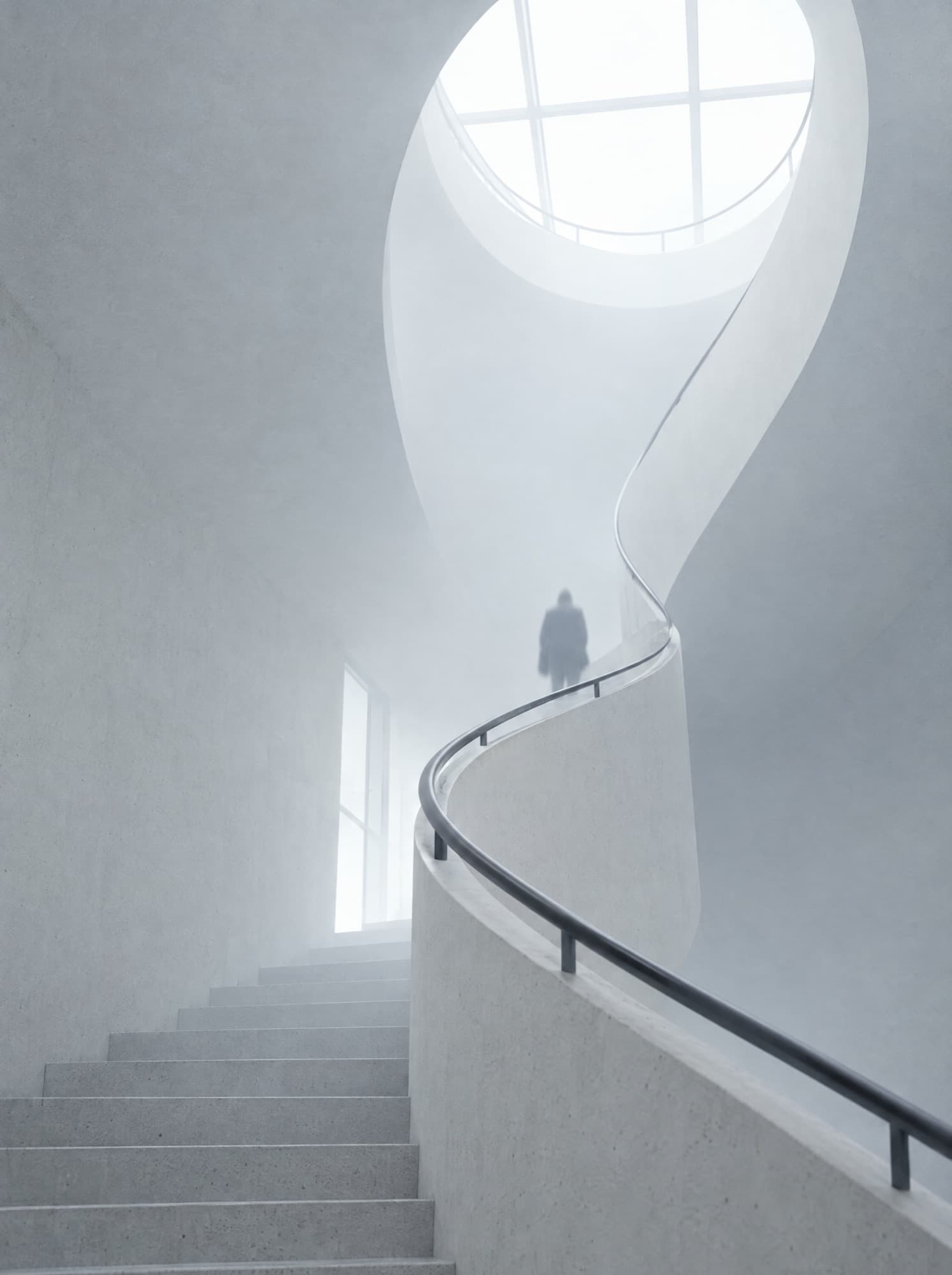 A white concrete stairwell rising toward a skylight